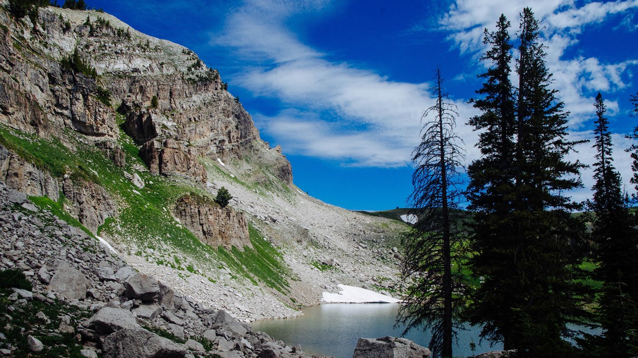 An alpine lake sits at the base of a rocky cliff.