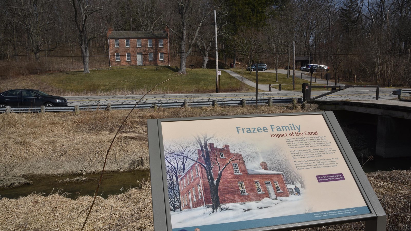 “Frazee Family” panel; behind it, across a water-filled canal and a road, a historic brick house.