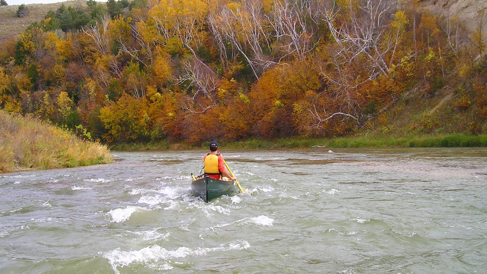 A river in fall with a canoer going over whitecaps.
