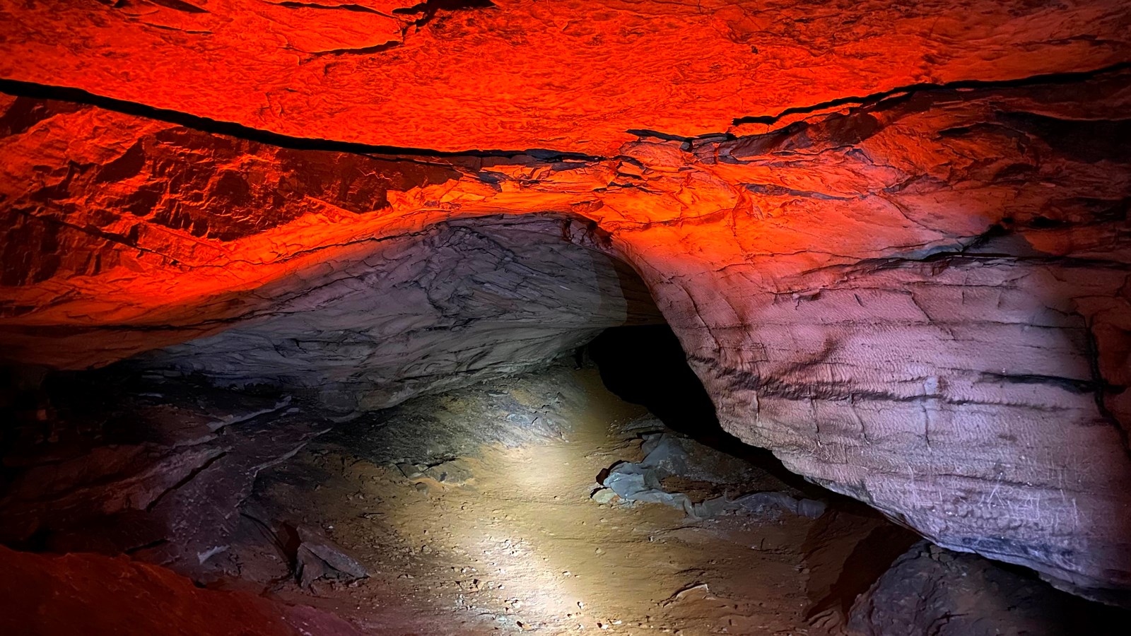 The opening of a cave passage lit up with a orange glow on the rock.