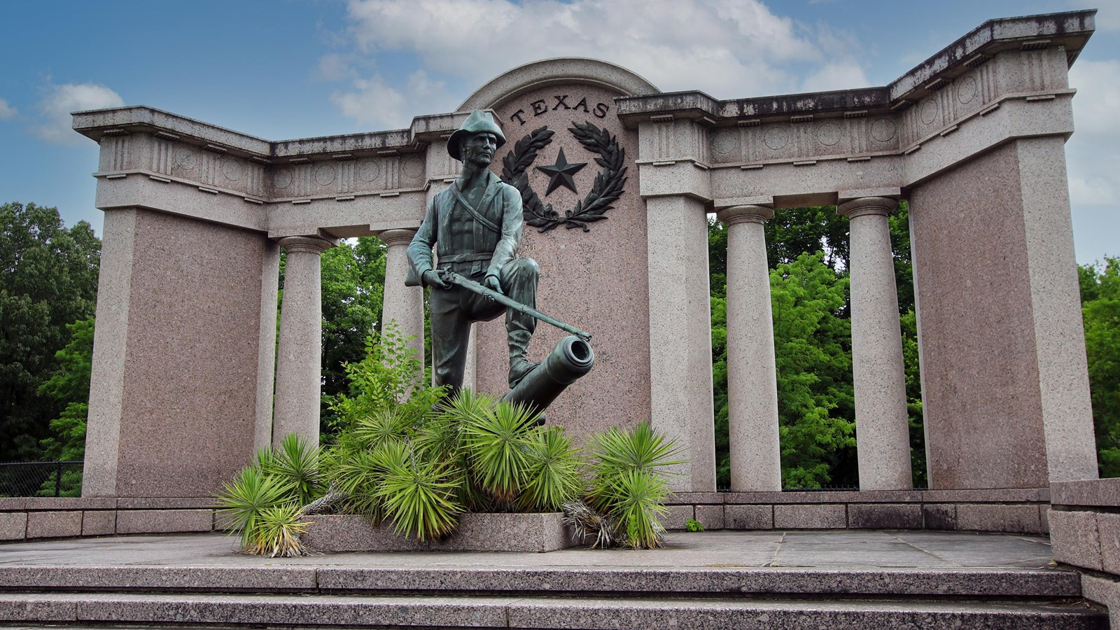 A single bronze stature holding a musket stands on a cannon barrel with a Texas shield behind it.