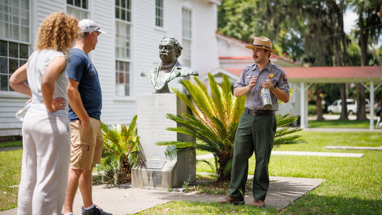 A ranger talks to two visitors in front of a bust of Robert Smalls.