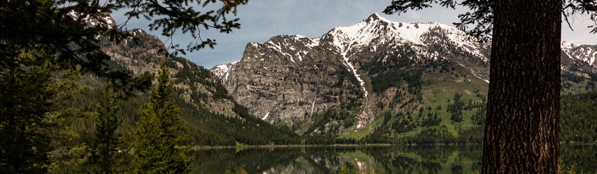 A wooden bench sits beside a lake surrounded by mountains.