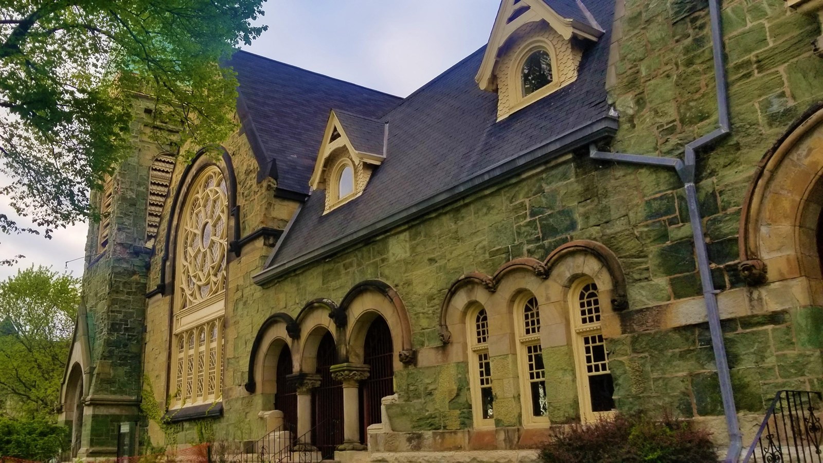 Green church facade showcasing rose window, front door arches, and steeple. 