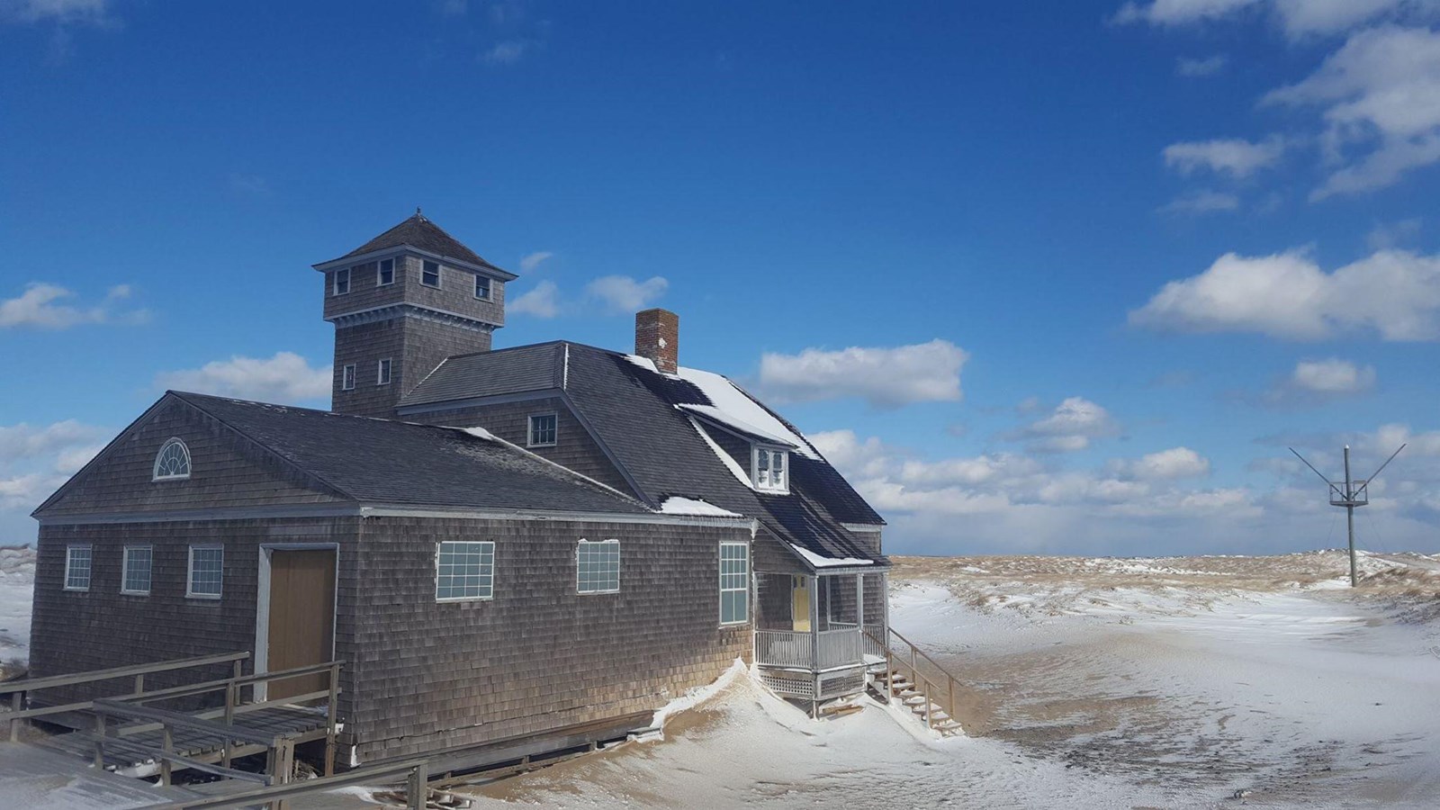 A historic building with a tower and cedar shakes stands against snow and a deep blue sky.