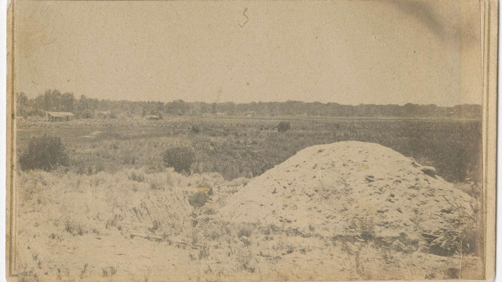 A black and white photograph of a large pile of dirt in an open field
