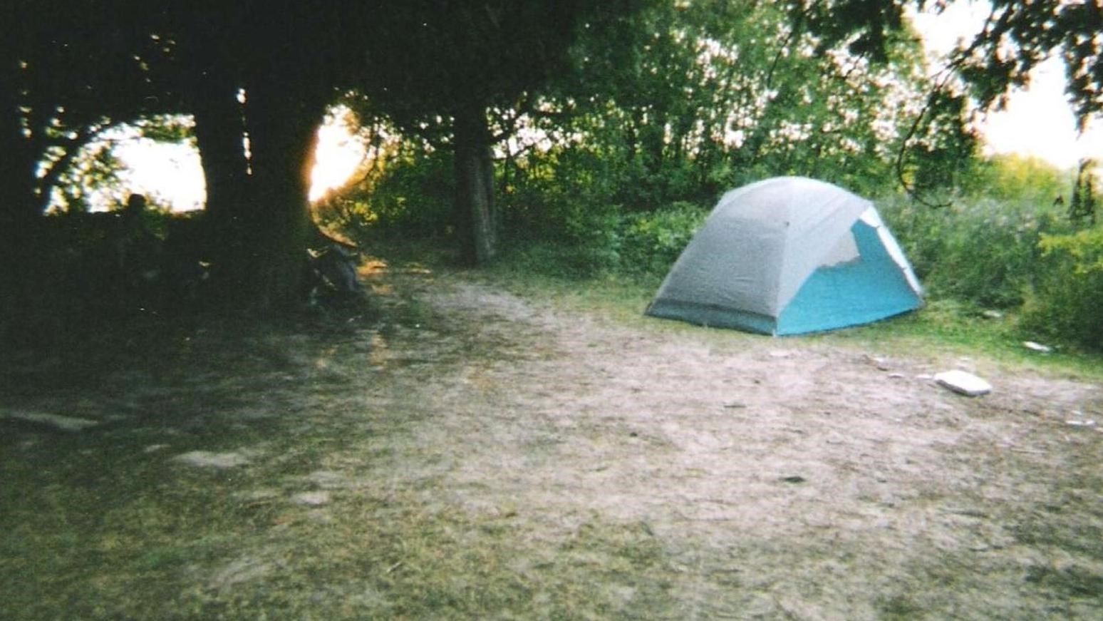 Small, blue tent pitched in a sandy opening surrounded by green trees