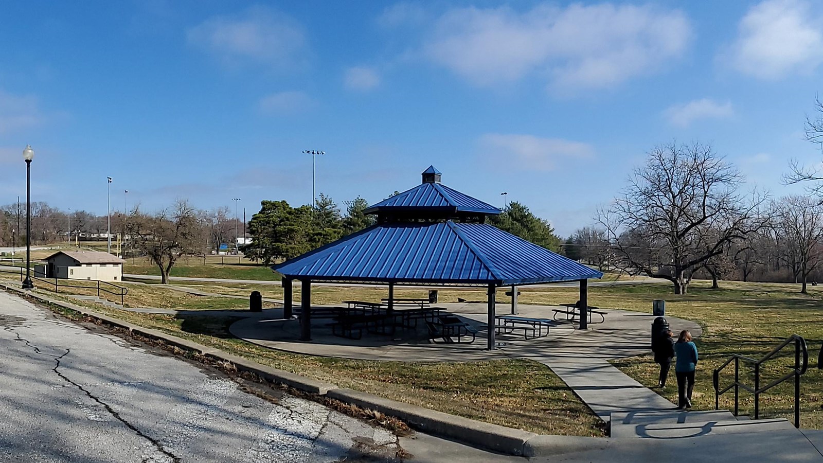 A picnic shelter with a blue roof, in a city park, under a blue sky.