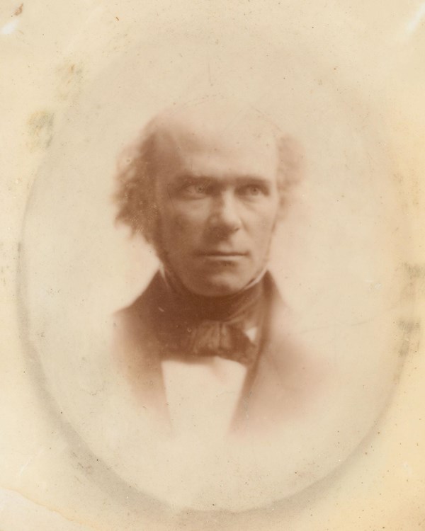 Sepia-toned photo of a White balding man wearing a suit, with light-colored eyes looking to the side