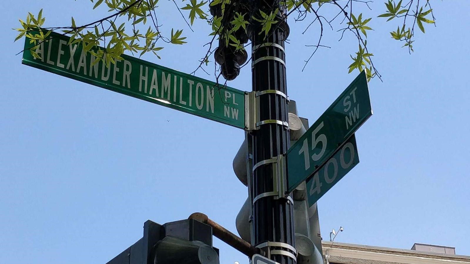Green street signs for the intersection of 15th Street and Alexander Hamilton Place.