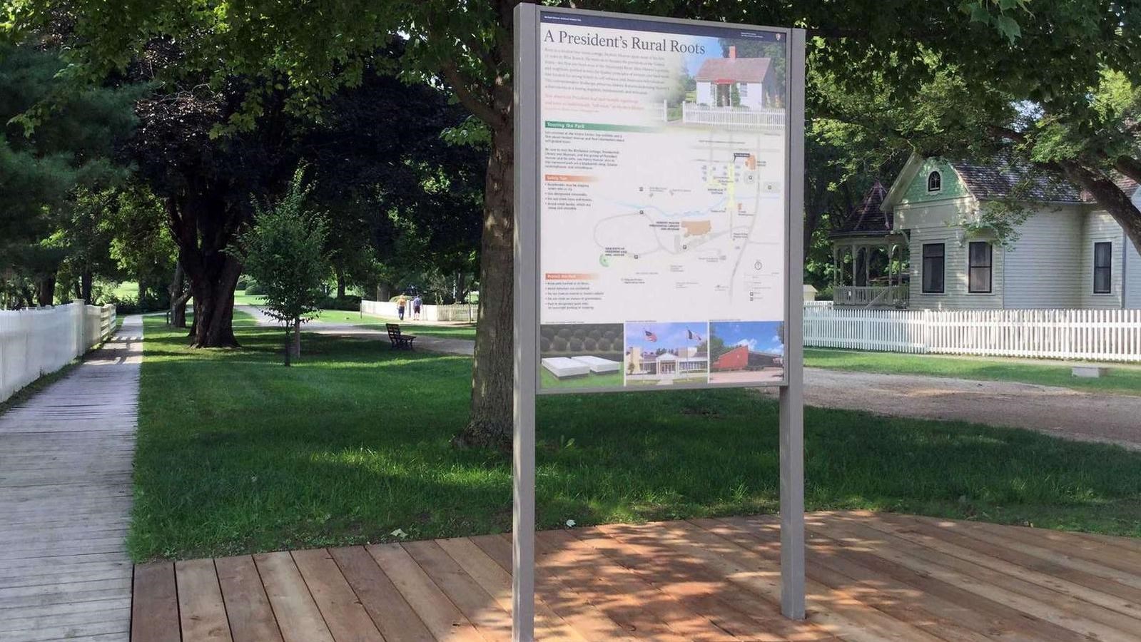An upright outdoor exhibit panel in a historic park displays a map, photos, and interpretive text.