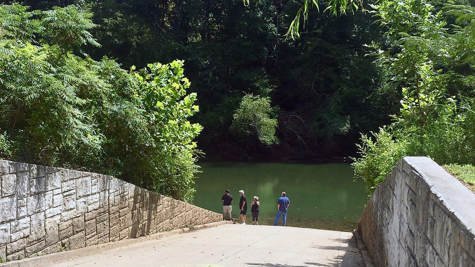 Looking straight down boat ramp with retaining walls on both sides and wood shoreline accross river.