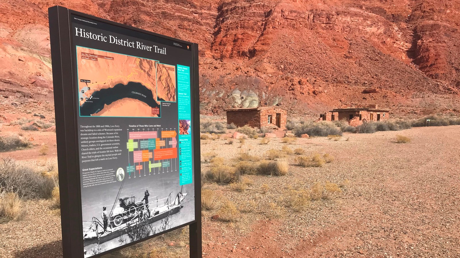 Trailhead sign with images of old ferry boat and trail map, historic buildings in the distance.