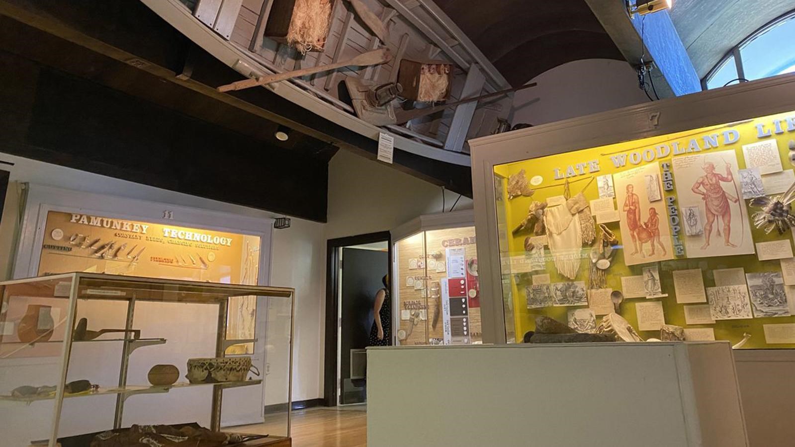 A native-built canoe hangs in a building over museum exhibits.