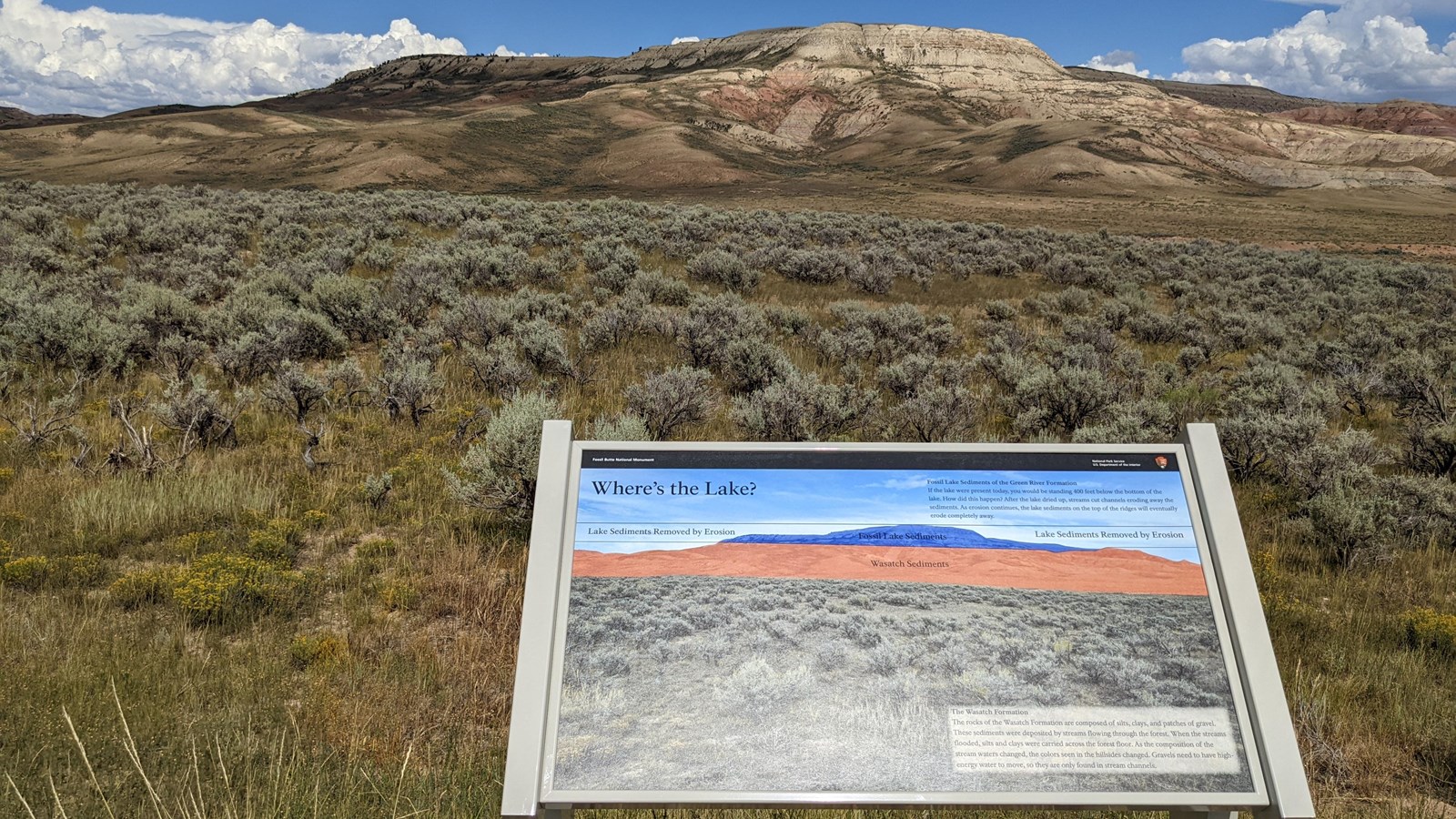 A sign with a photo of the butte colored blue and red. The butte is visible behind the sign.