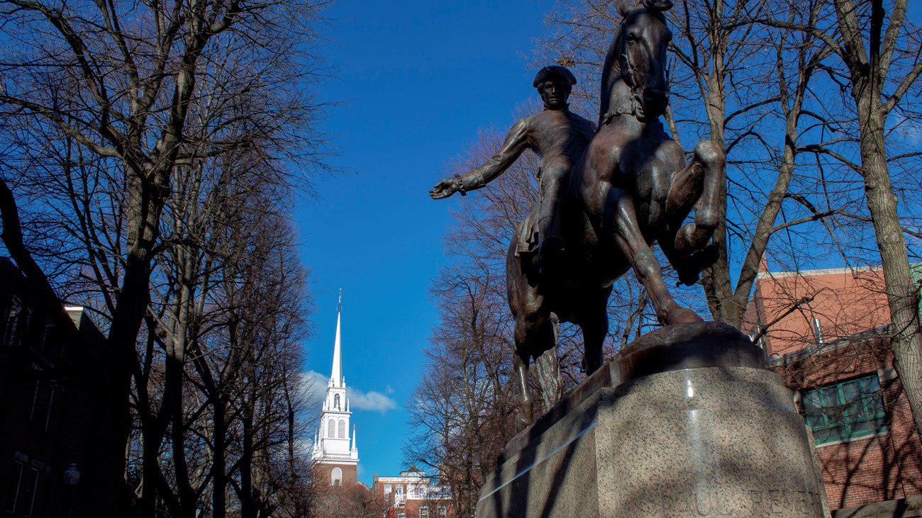 Statue of a man on horseback waving his arm. In the background is a white steeple.