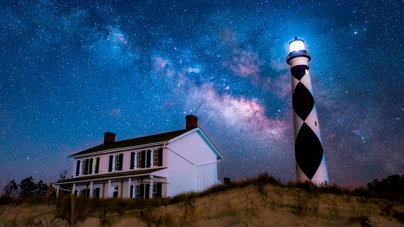 The Milky Way arches across the night sky above the Cape Lookout Lighthouse and Keepers\' Quarters