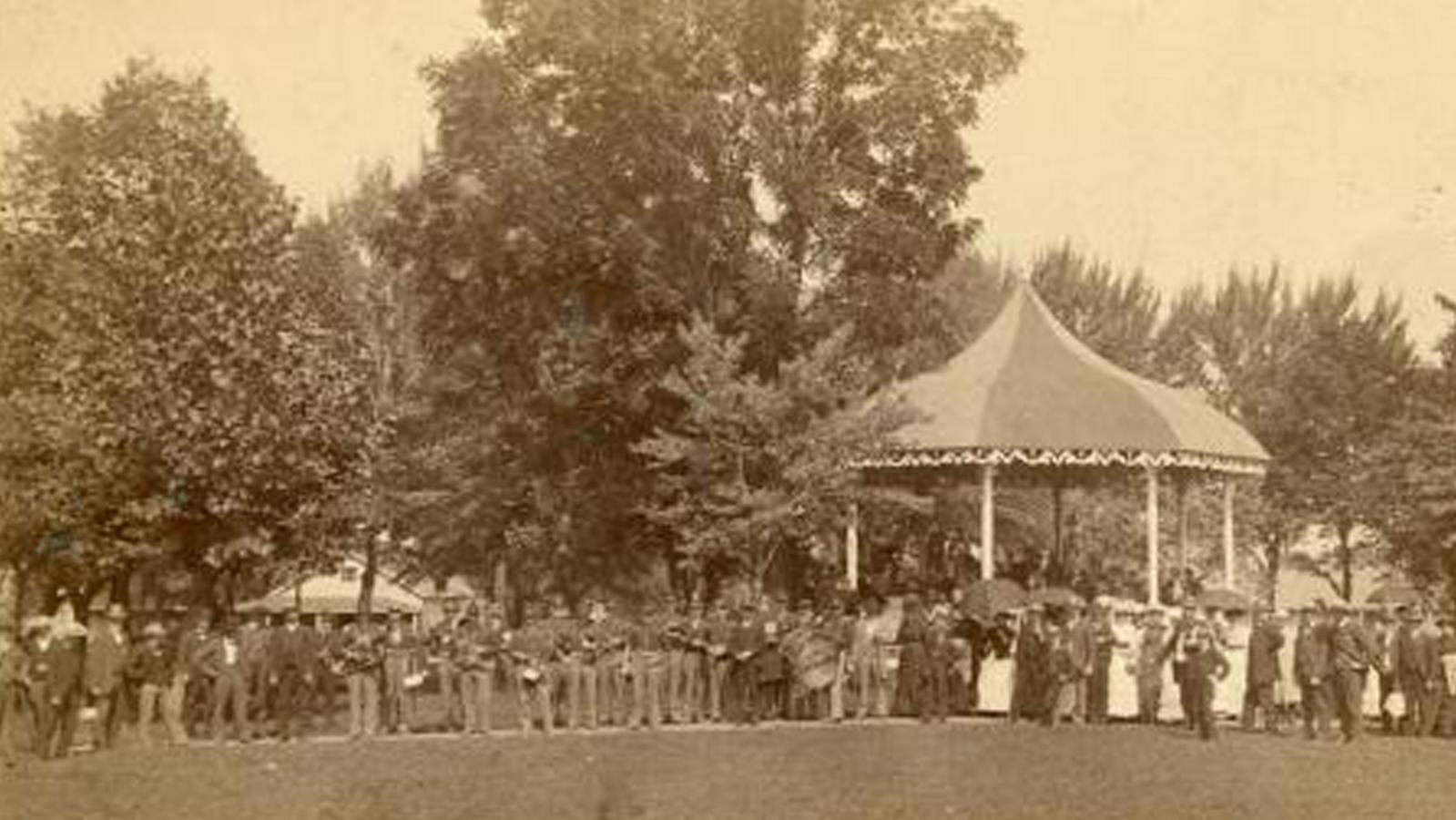 An historic photo of a circular bandstand platform with a large crowd in front of it.