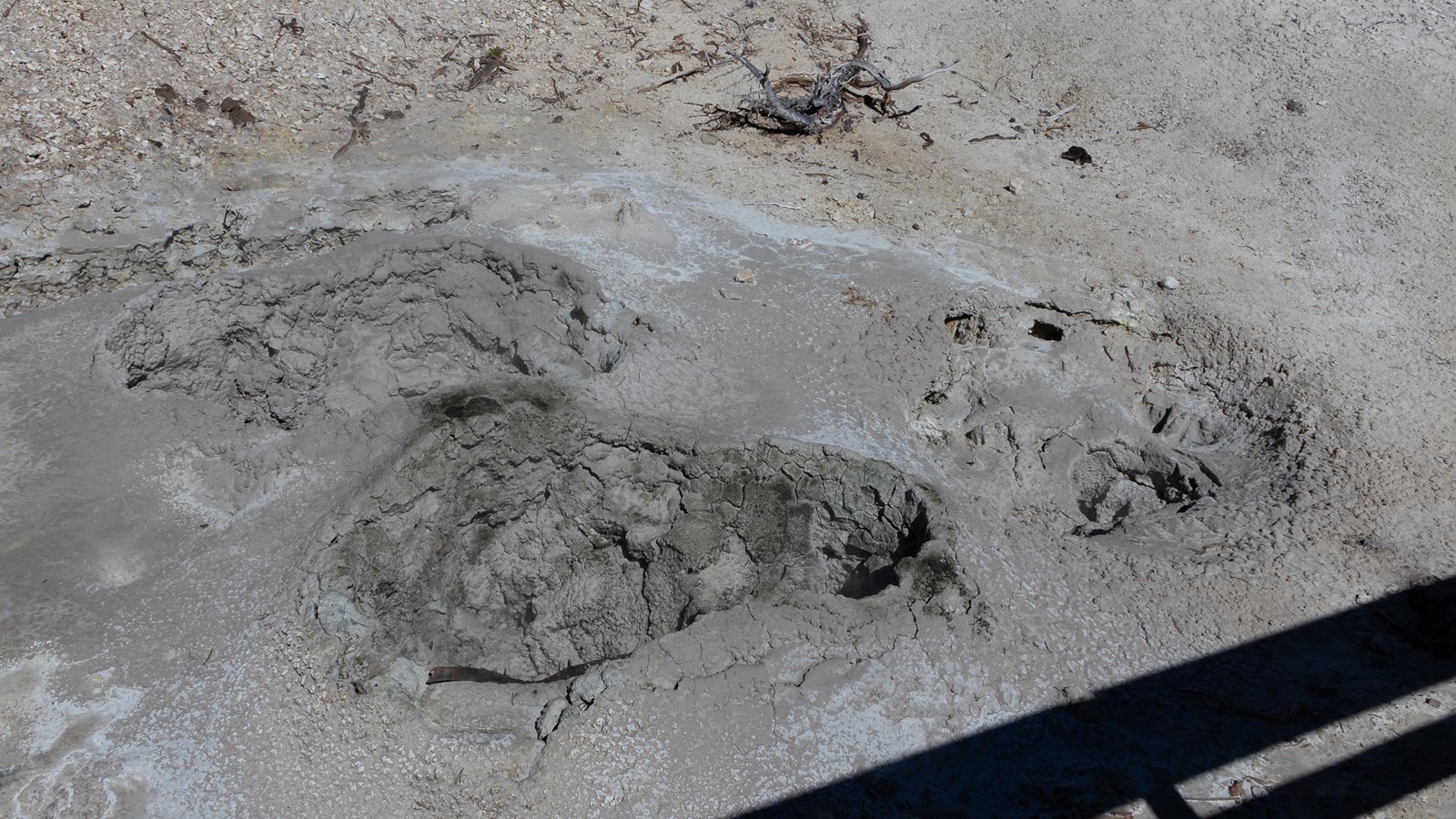 Three steam vents located in dry, cracked mud.