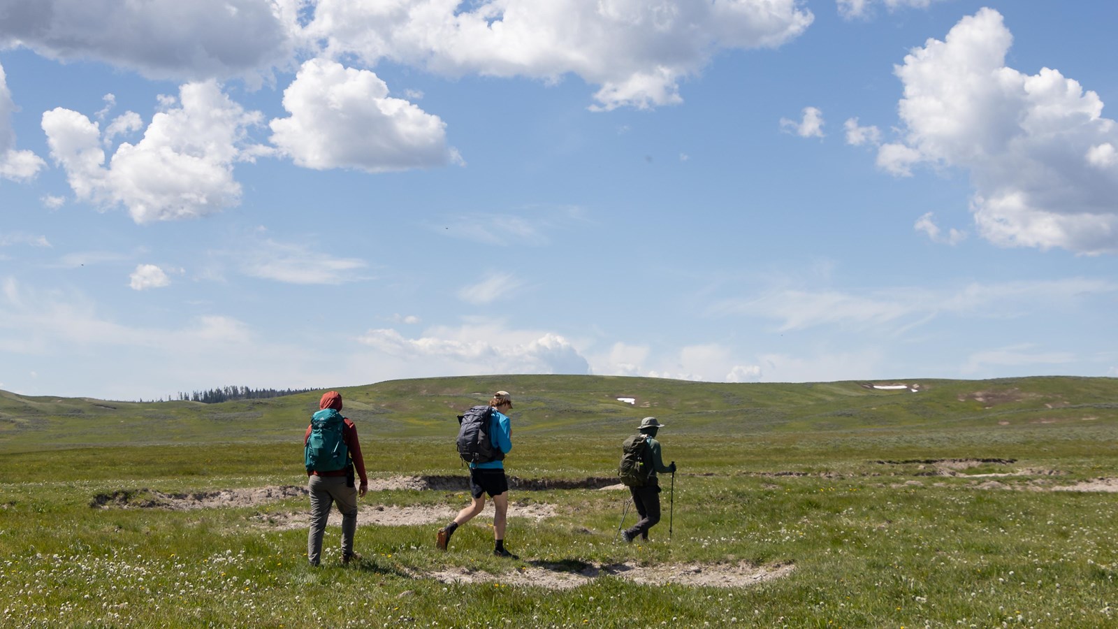 Three people walk across a large, green valley.
