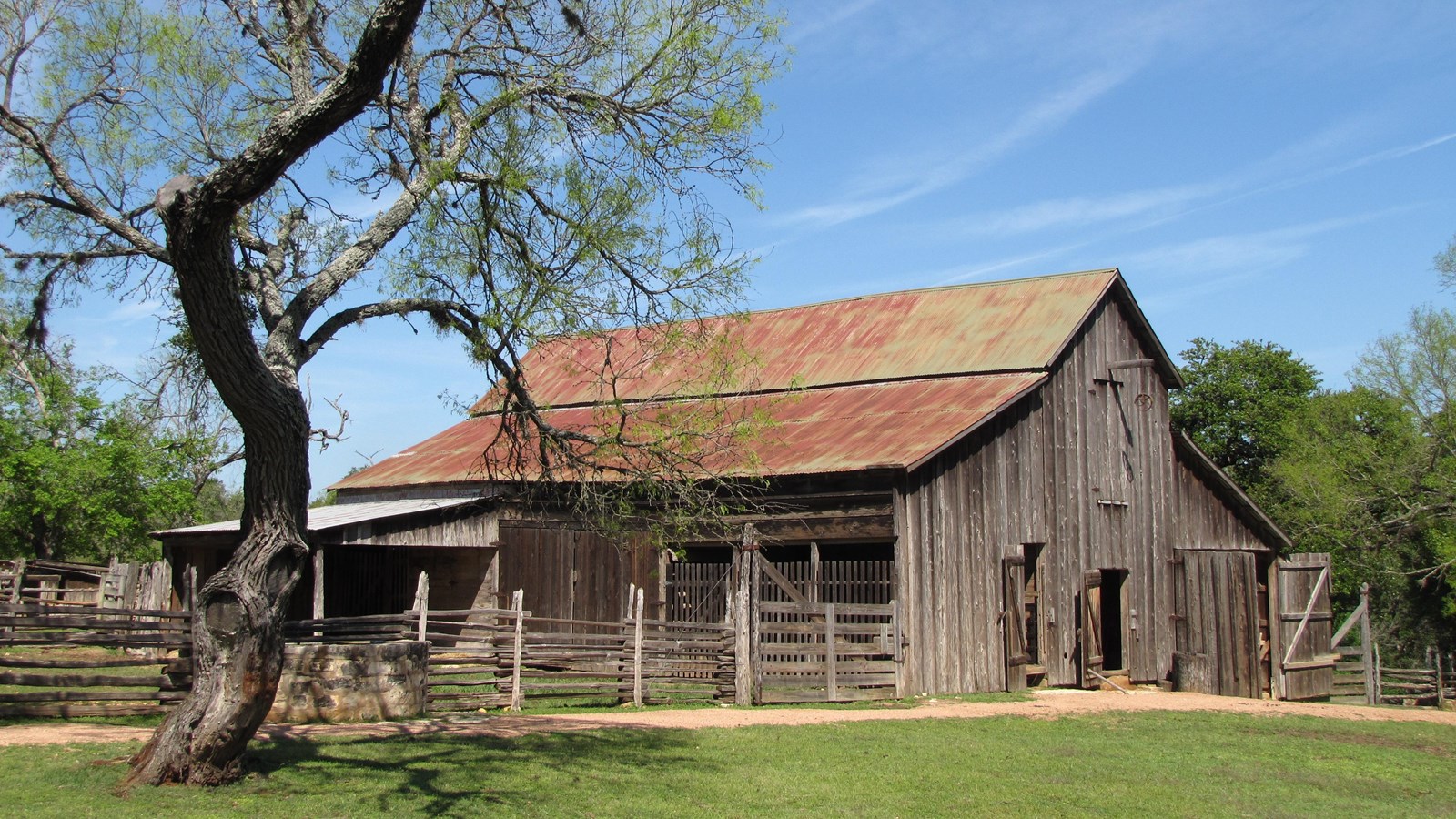 A large, wooden barn with metal roof has connected lean-tos and fenced area.