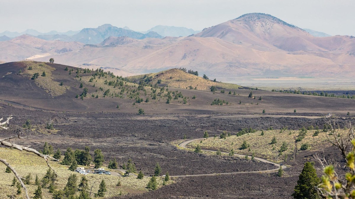 A narrow road winds through a volcanic landscape, ending at a small parking area.
