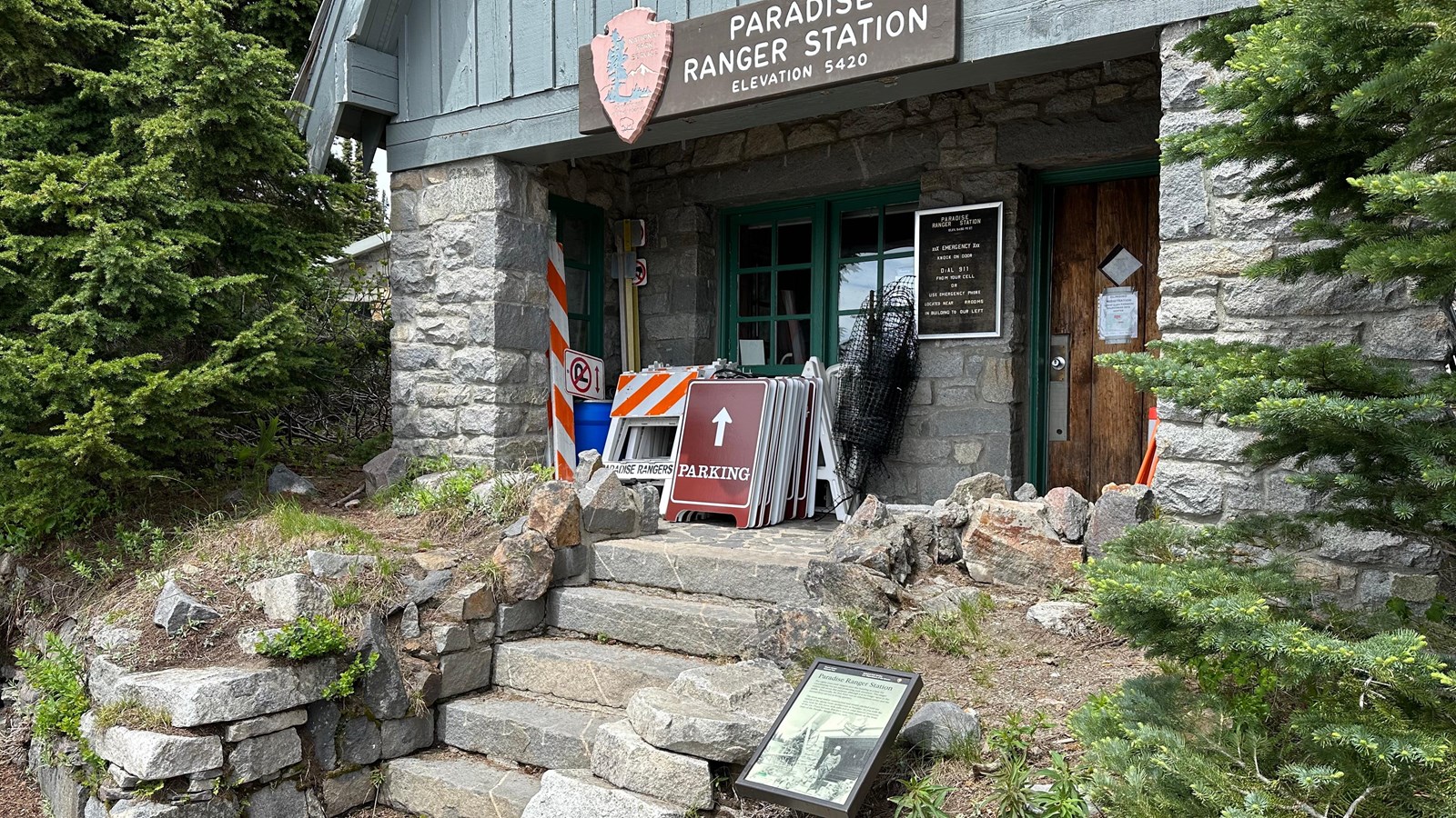 An exhibit panel on the right side of stone steps leading up to a small building a covered porch.