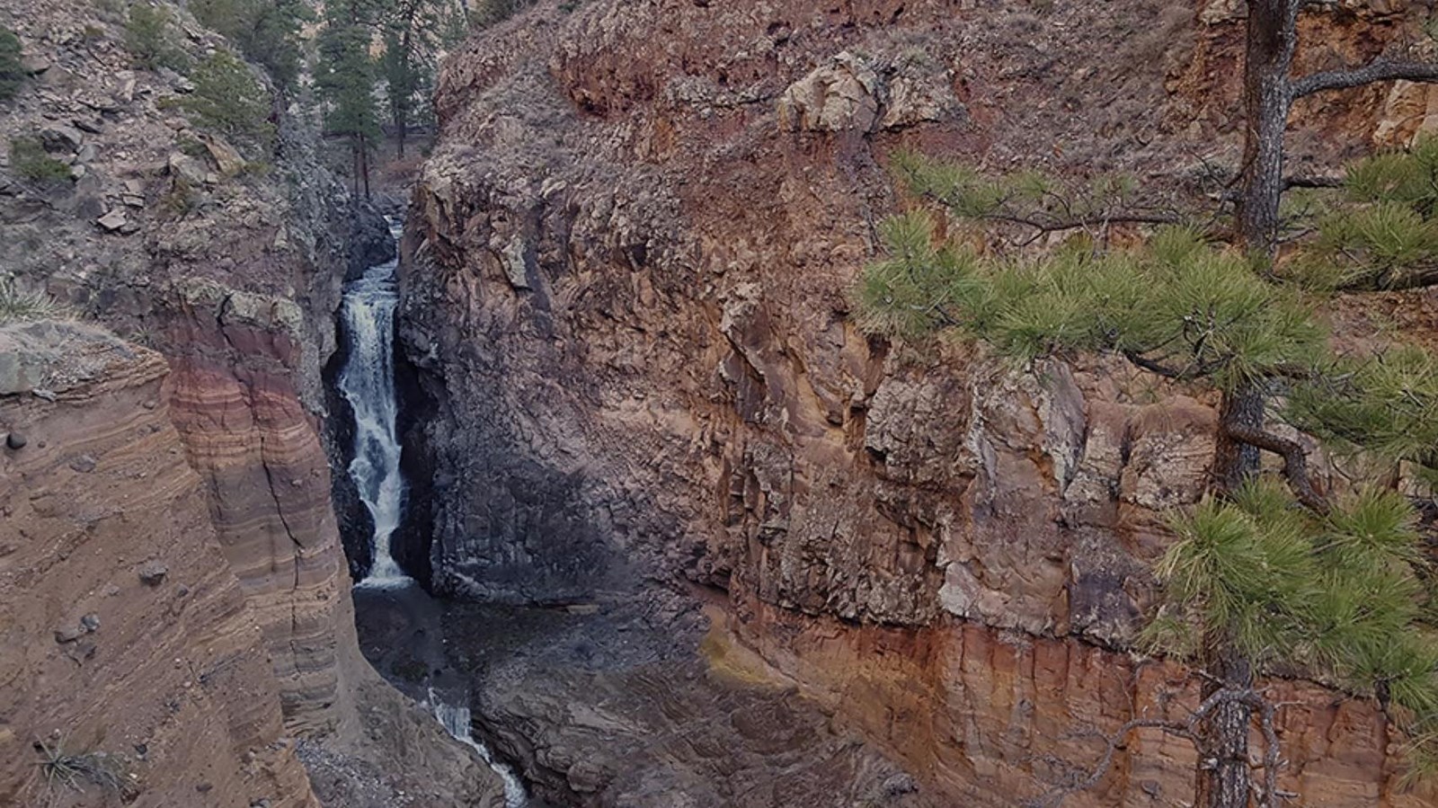 A thin, 80-foot waterfall pours down a crack in layered orange and brown cliffs.