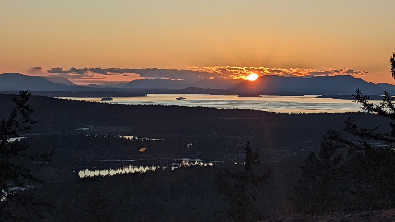 A view of a sunset from the top of a mountain, looking towards the ocean and islands.