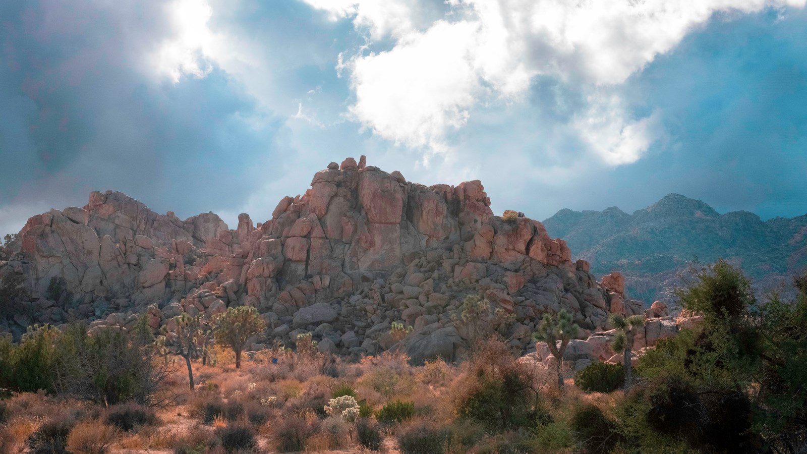 A large rock formation with mountains in the distance under dark storm clouds.