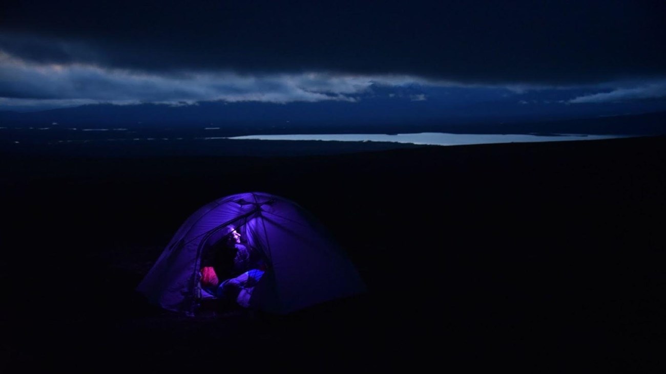 A night time scene of a woman in a tent with her headlamp glowing up the walls. 