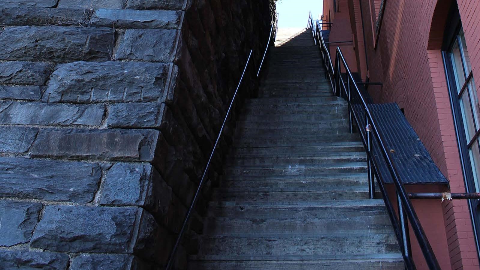 Long, narrow, steep staircase. A building on one side and a retaining wall on the other side