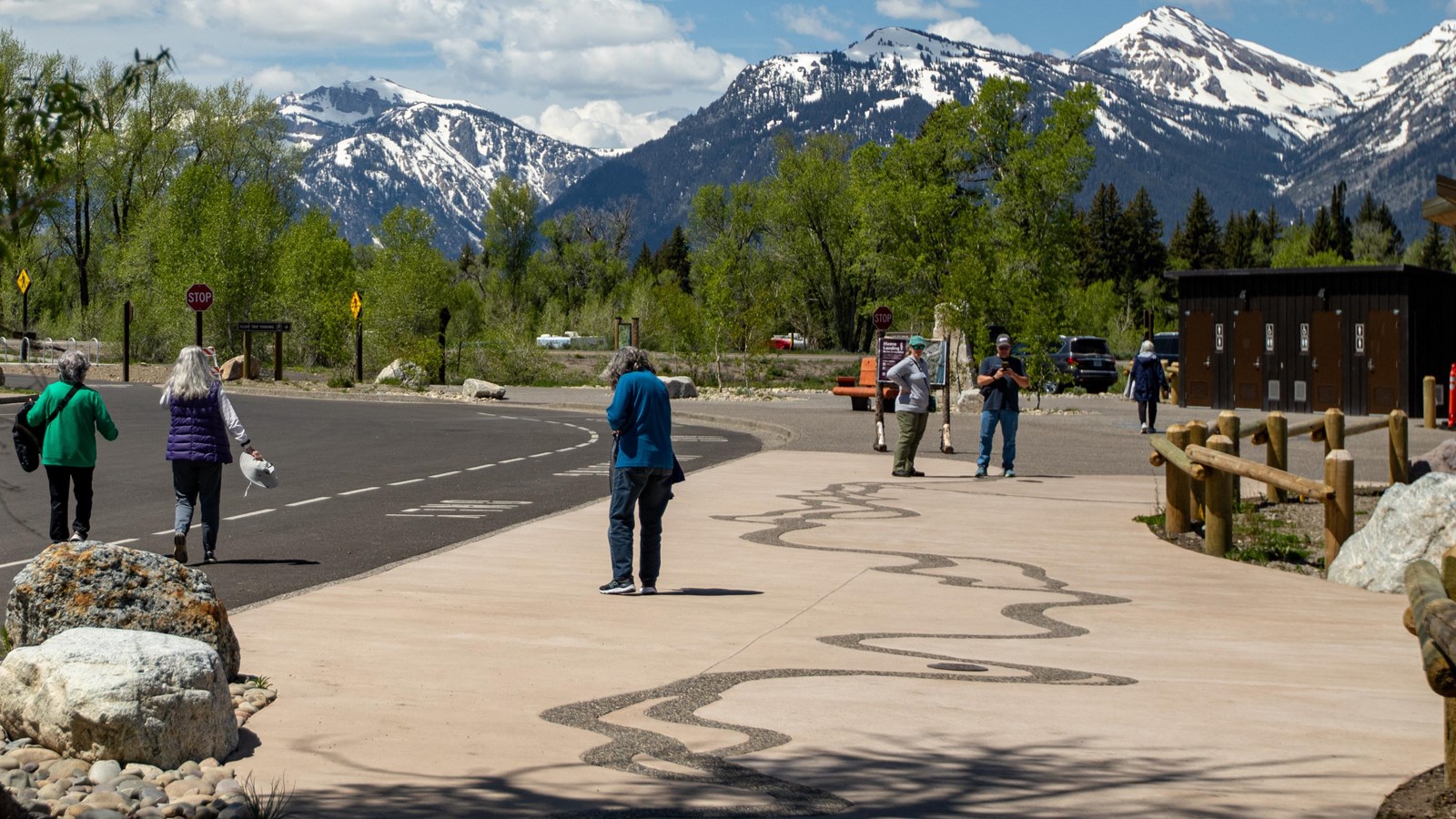 Multiple visitors walking on the sidewalk near restrooms. Trees and mountians in the background. 