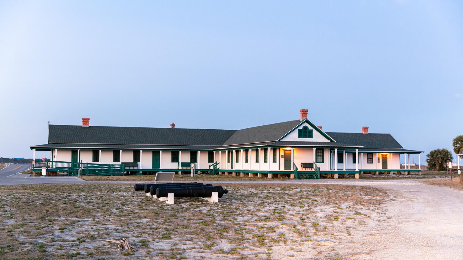 A white and green building stands with cannons in the foreground.