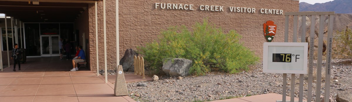 A large stone building with a white awning covering the entrance. A digital thermometer is outside.