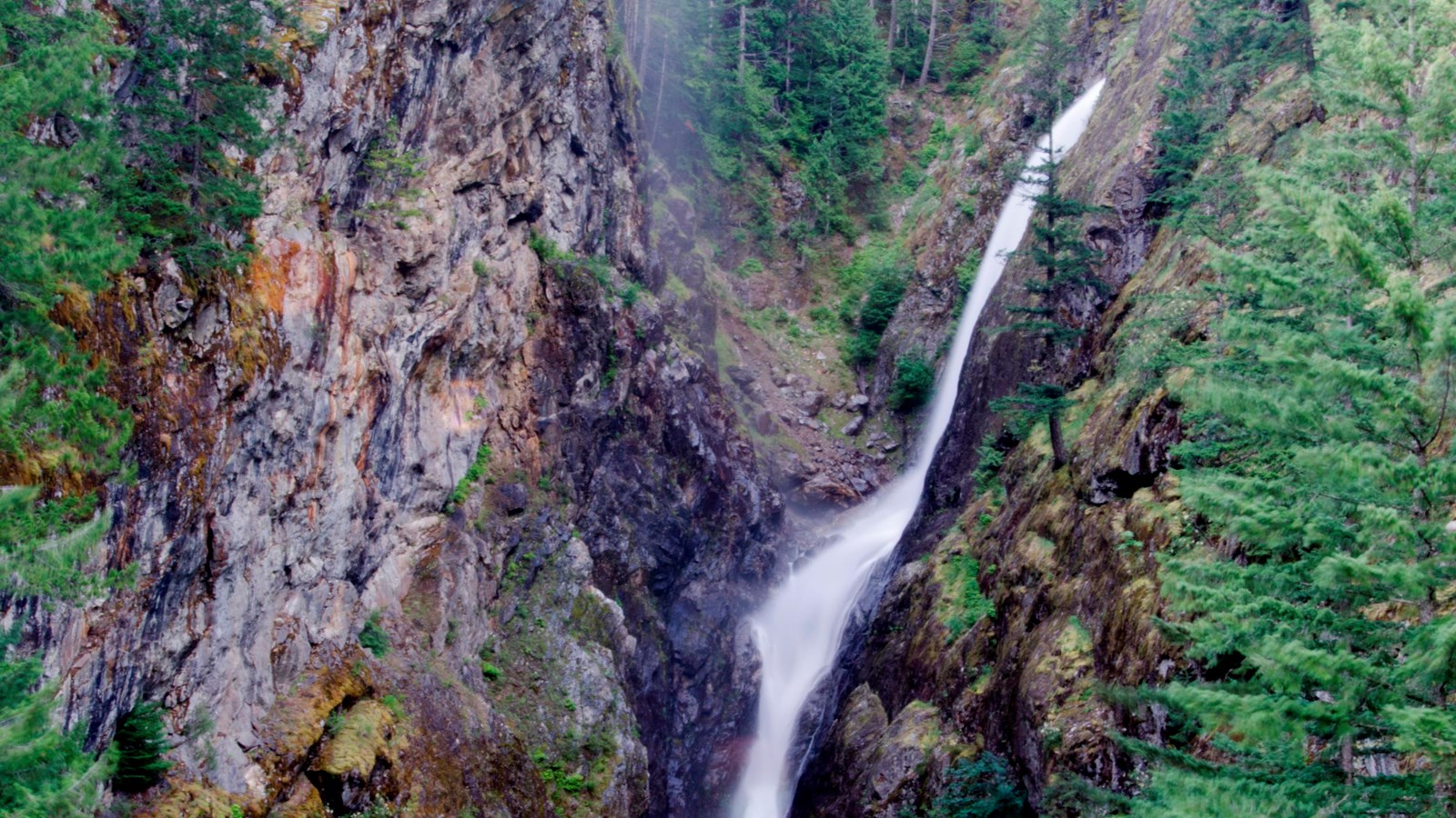 A waterfall flows through a steep, rocky gorge.