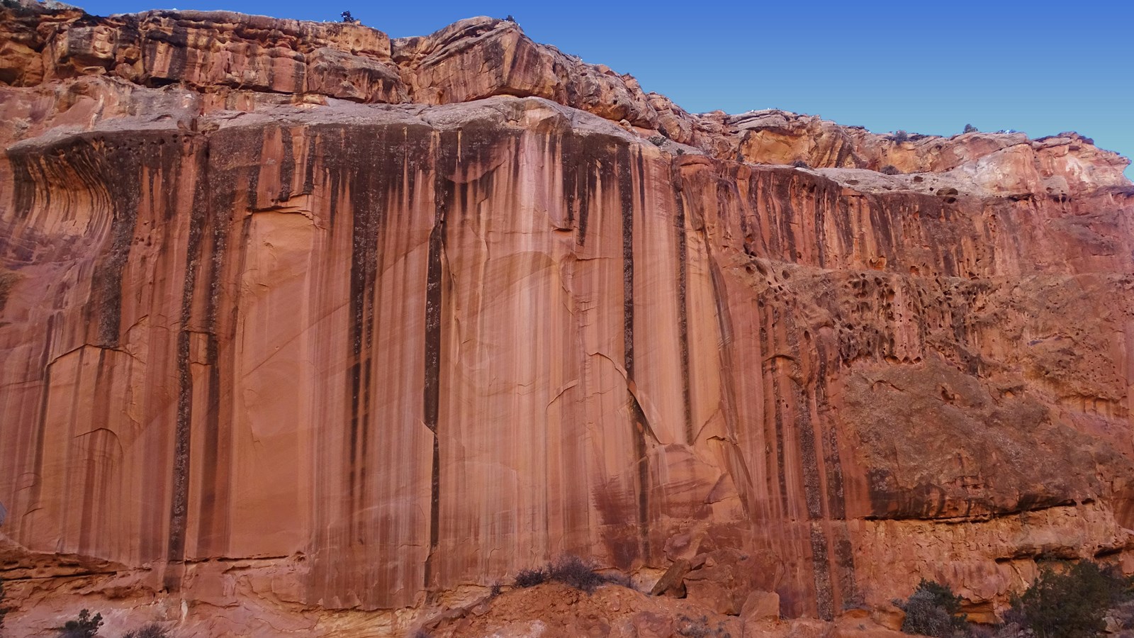 A sheer red-brown cliff about 500 feet tall with black vertical streaks.