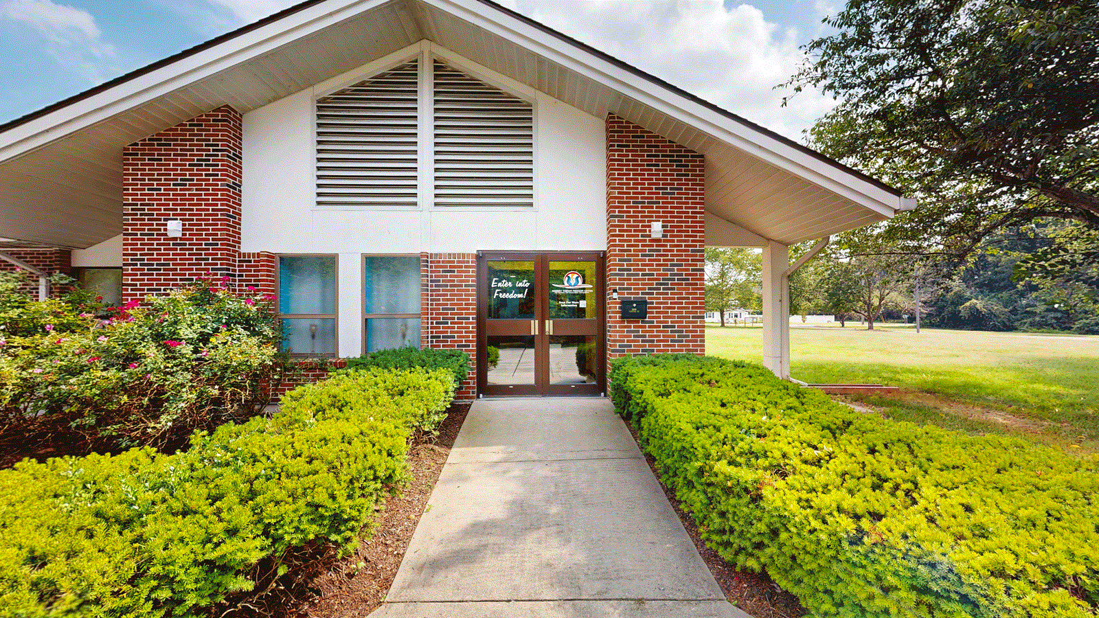Front view of a brick building with glass doors and surrounding shrubs.