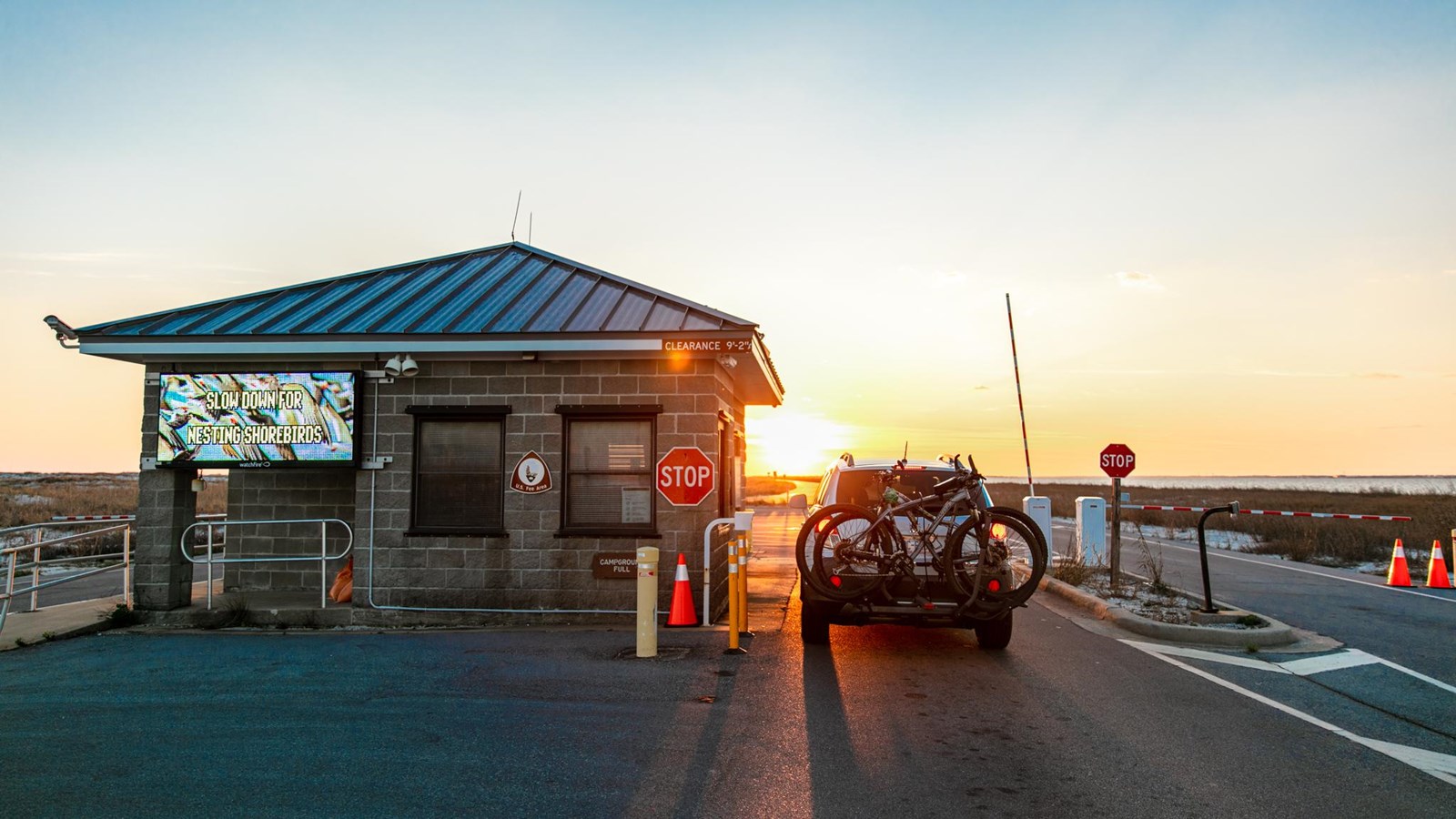 A car enters an entrance station gate at sunset.
