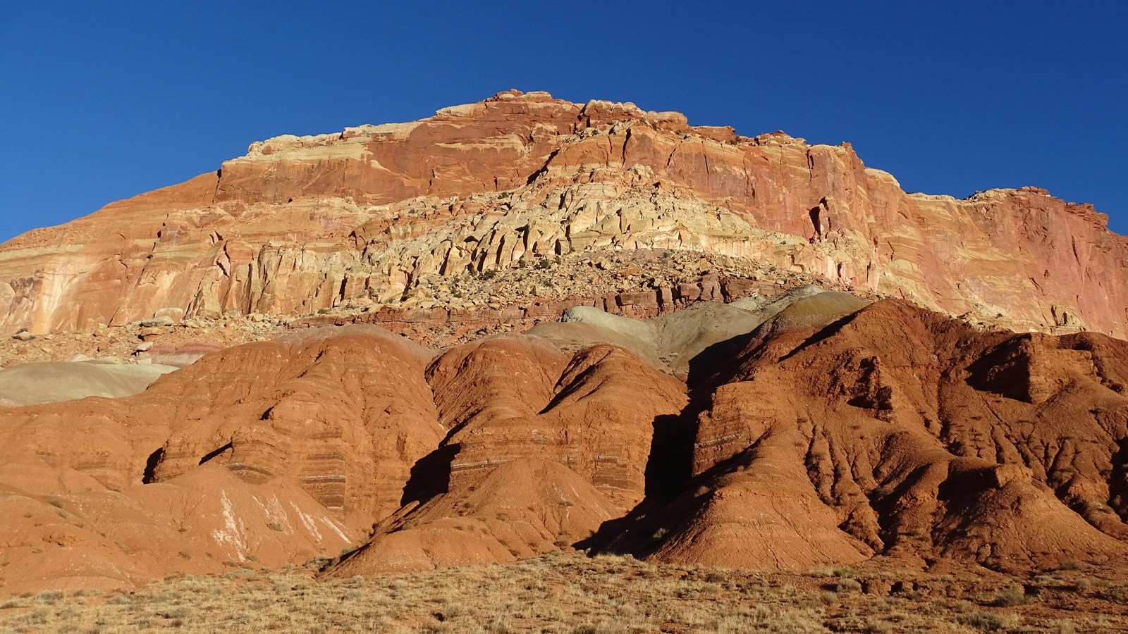 Red-brown cliffs about 500 feet high with sloping soft rock at the base.