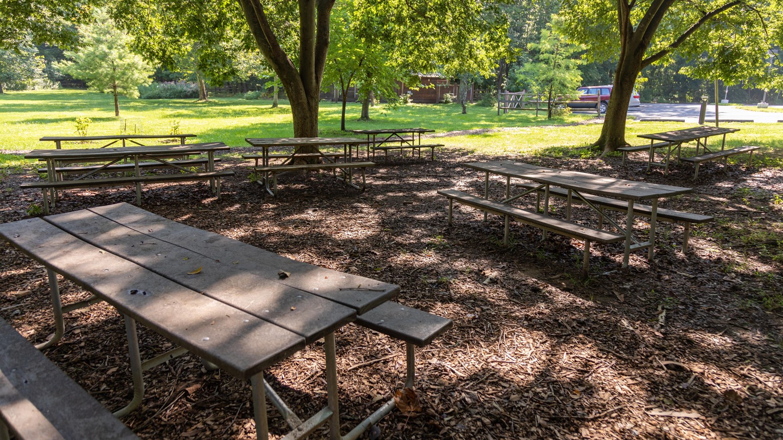 Picnic tables under trees with a brown building with restrooms.
