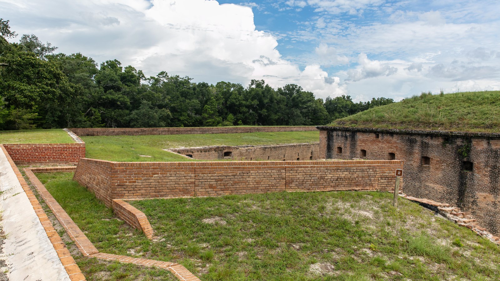 A brick wall that formed a traverse stands atop a grassy plain in a fort.