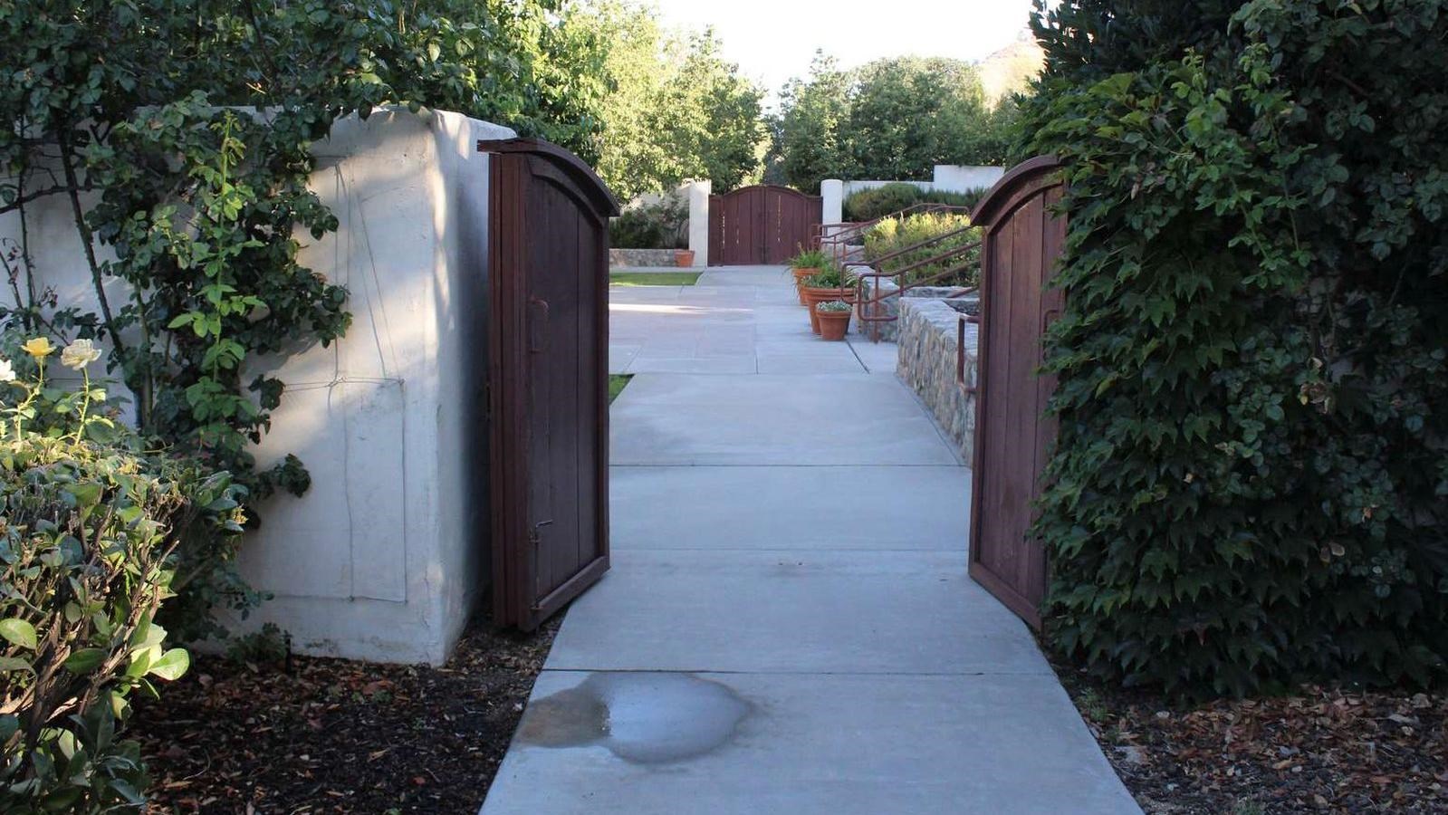 An outdoor cement pathway leading through two wooden doors.