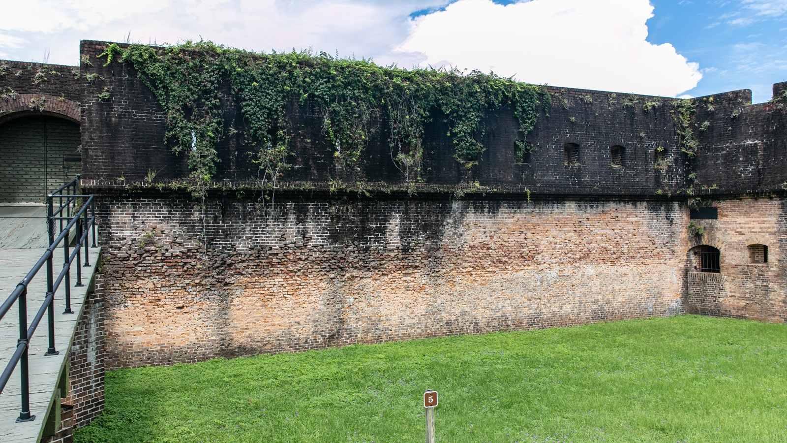 A brick wall with a drawbridge to the left is covered in small dents and pits from target practice.