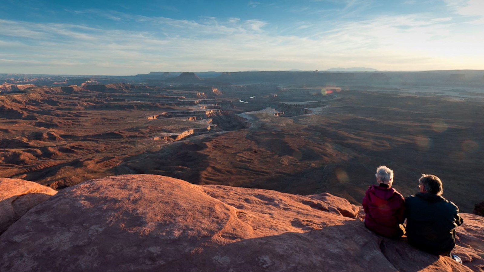 Two hikers sit on the edge of Green River Overlook at sunset