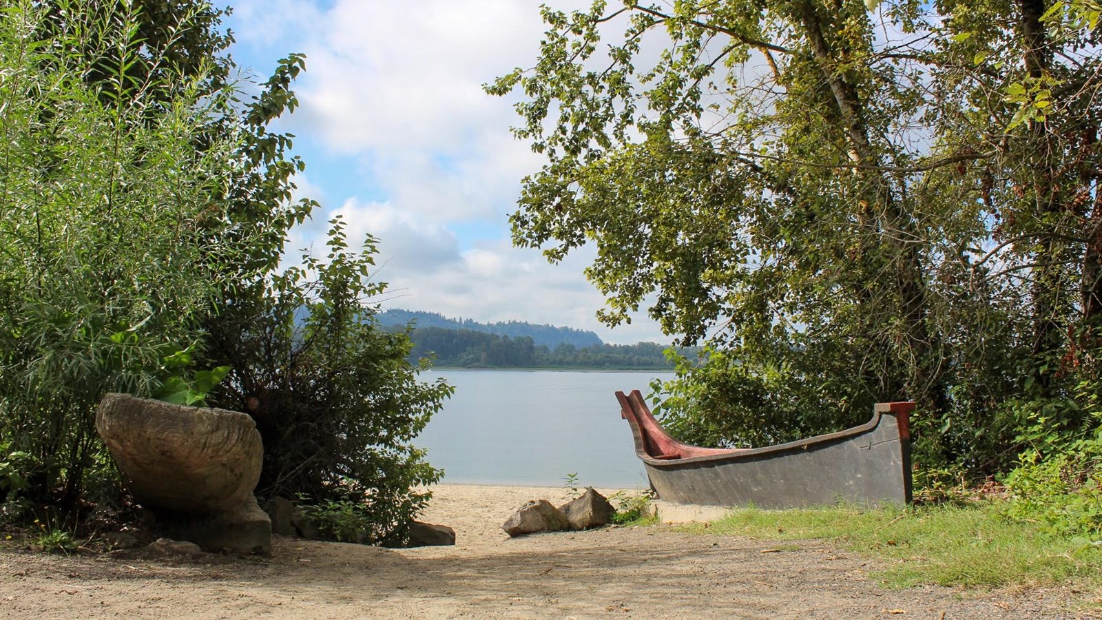 A replica early 19th century canoe sits at the edge of a river surrounded by trees