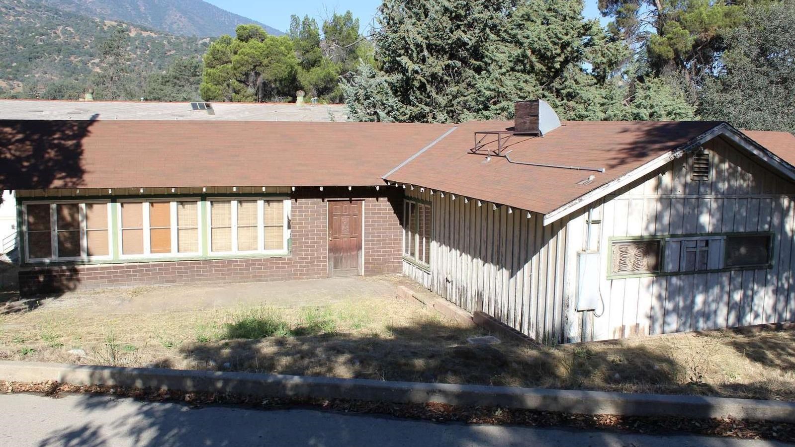 A worn building made of red brick and white wooden panels with a brown roof.