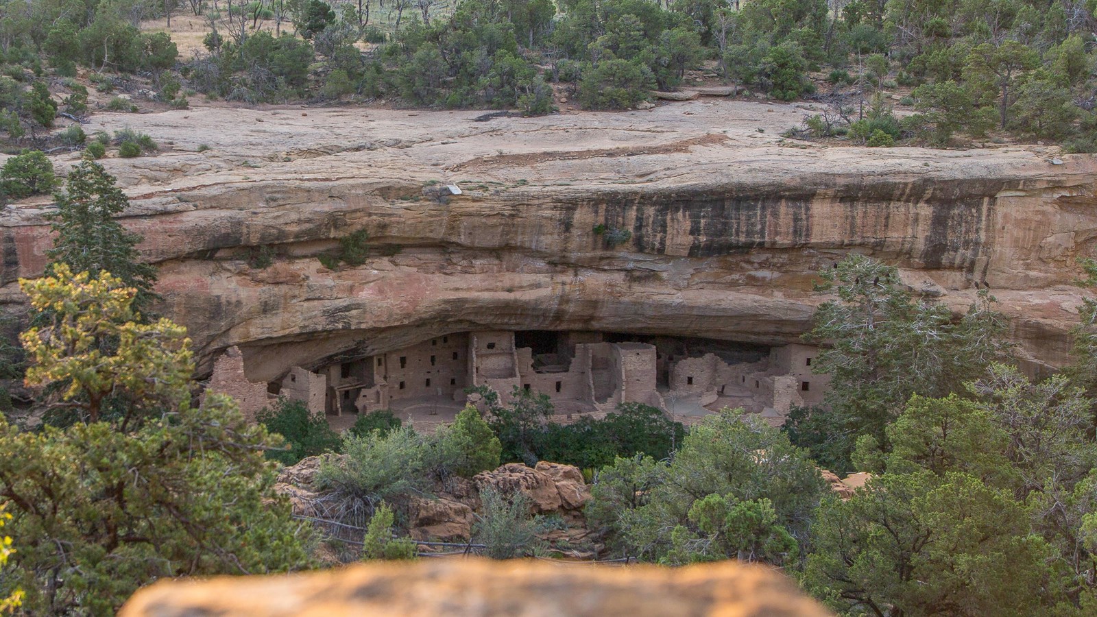 Looking across narrow canyon at ancient, stone-masonry village tucked in an alcove.