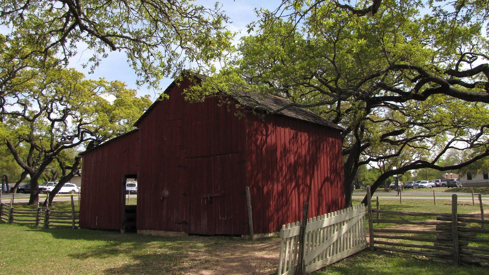 A wooden, two-story, red barn is framed by long, live oak branches.