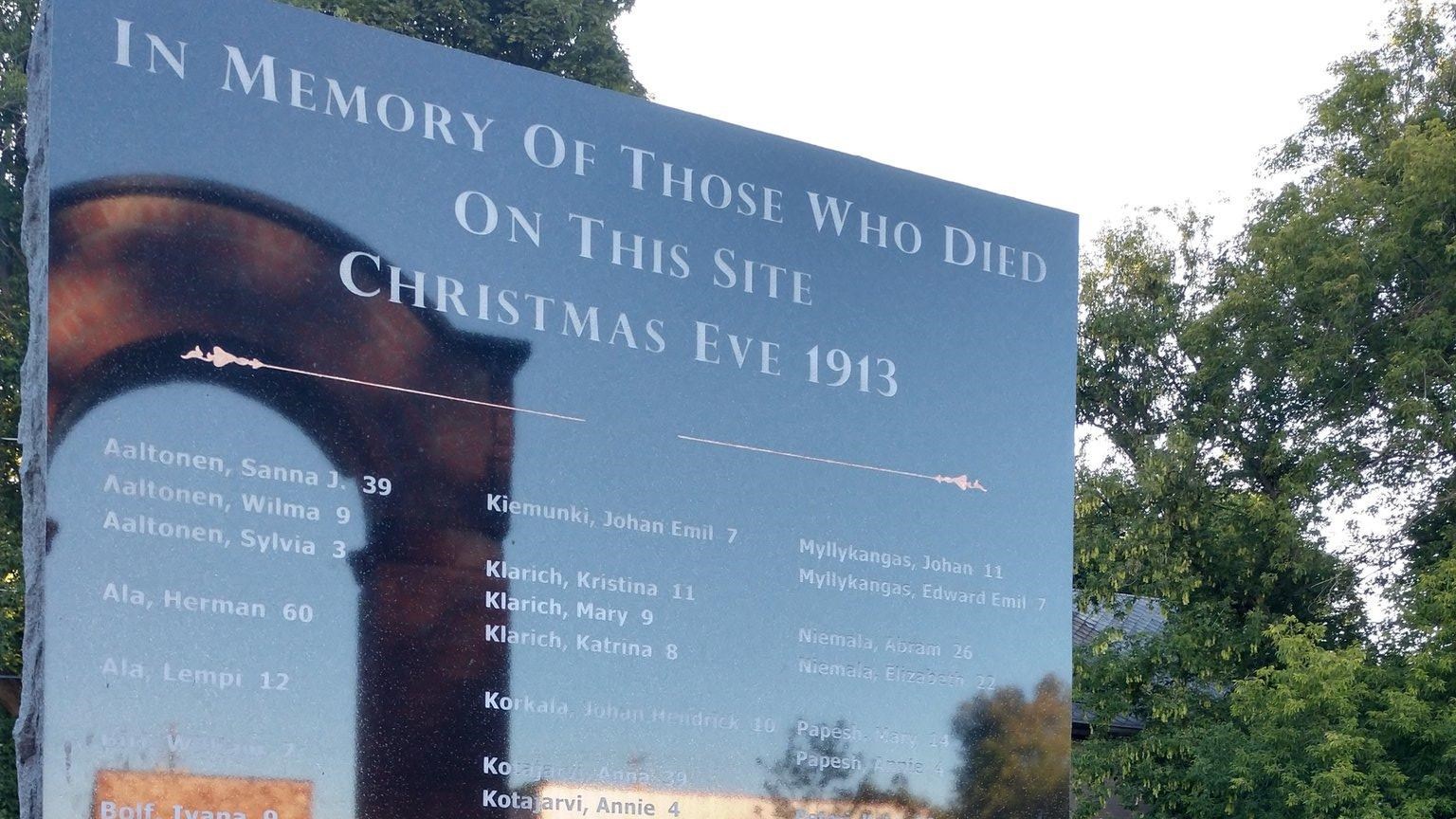 A stone memorial with a reflection of the Italian Hall arch